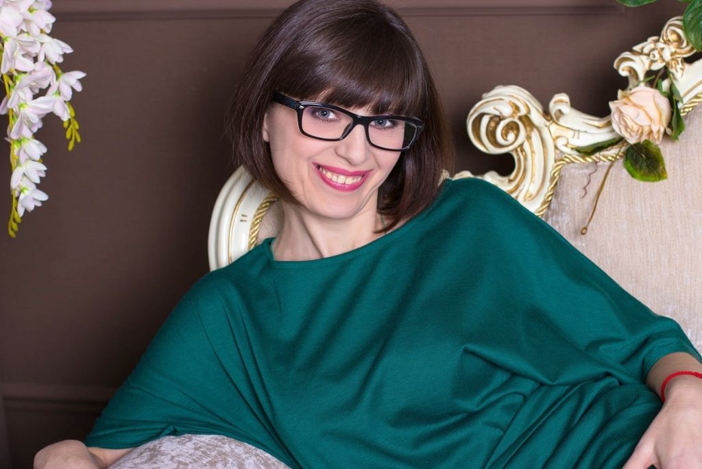 Oral majstor, atraktivna brineta srednjih godina pozira u kratkoj svilenoj haljini na kauču