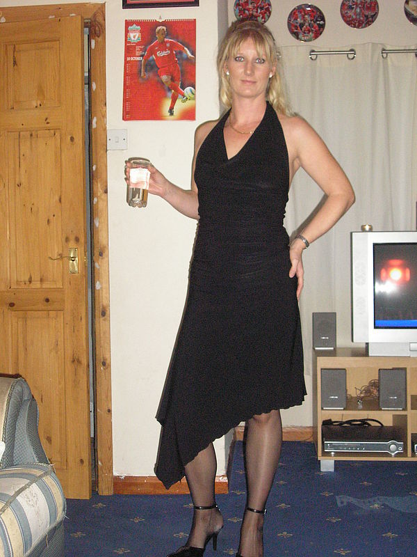 Izazovna plavuša pozira u crnoj dugoj haljini sa čašom vina u ruci