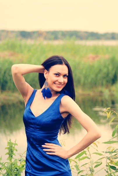 Nasmejana lepa crnka pozira kraj jezera u uskoj plavoj haljini