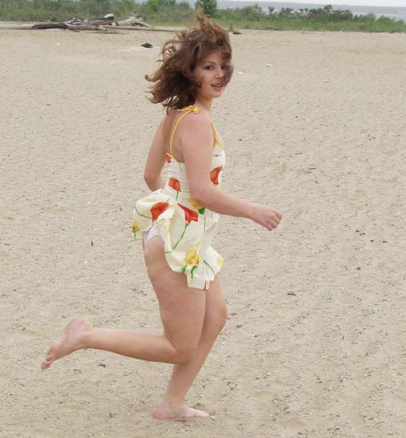 Slatka devojka trči na plaži u kratkoj haljini
