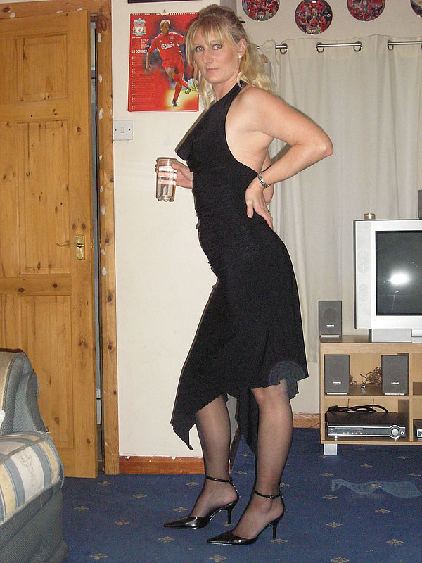 Izazovna plavuša pozira u crnoj dugoj haljini sa čašom vina u ruci