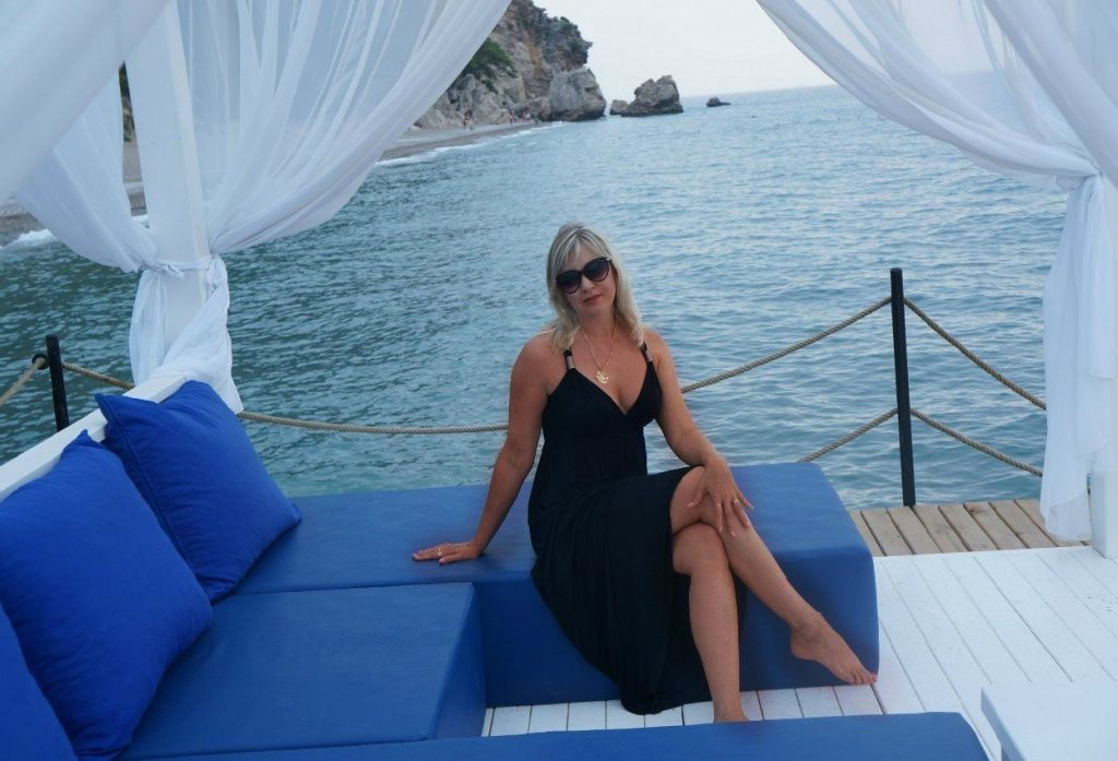 Zabavna zgodna plava žena pozira na plaži u dugoj crnoj haljini