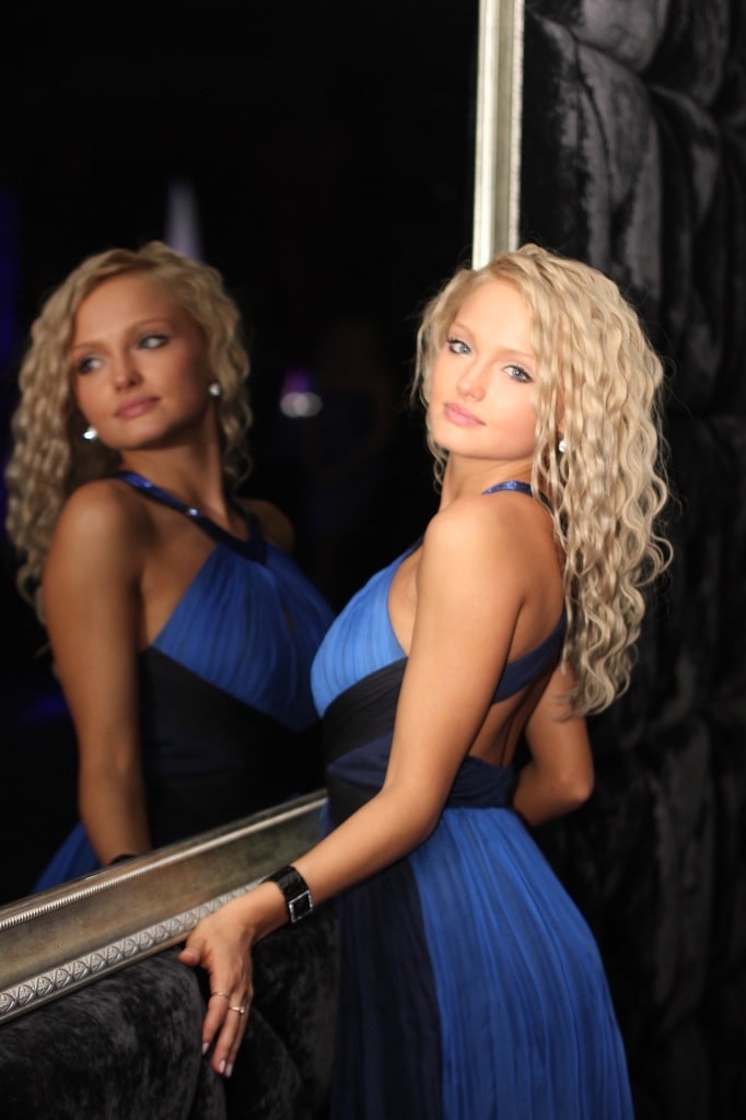 Seksi i raspoložena plavuša pozira nasmejana u elegantnoj plavoj haljini kraj ogledala